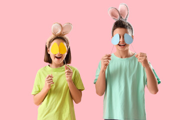 Happy little children in bunny ears with paper Easter eggs on pink background
