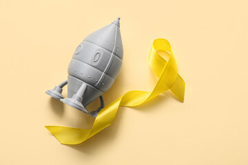 Golden ribbon with rocket toy on beige background. Children cancer awareness concept