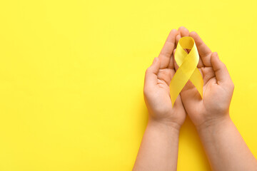 Hands with golden ribbon on yellow background. Children cancer awareness concept