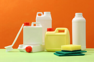 Set of different detergent canisters and bottles decorated with sponges and brush on orange background. Front view, advertising photo for cleansing product. Delicate and clean cleansing concept