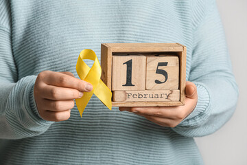 Woman holding golden ribbon and calendar on white background, closeup. Childhood cancer awareness...