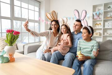 Happy family in bunny ears with Easter rabbits taking selfie at home
