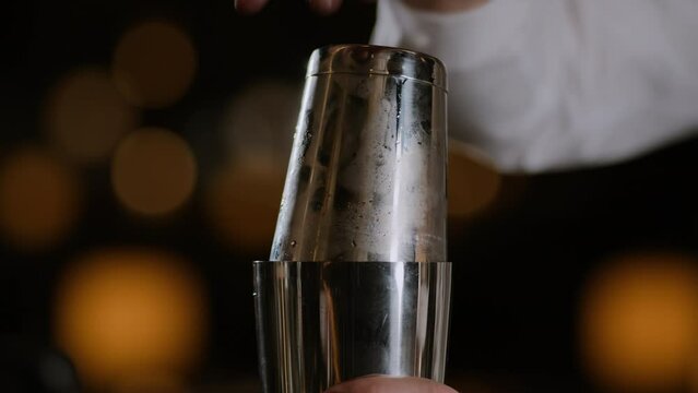 Closeup shot of a bartender closing up a cocktail shaker and beginning to shake cocktail