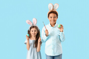 Little children in bunny ears with Easter eggs and paint brushes on blue background