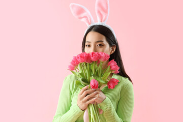 Young Asian woman in bunny ears with tulips on pink background. Easter celebration