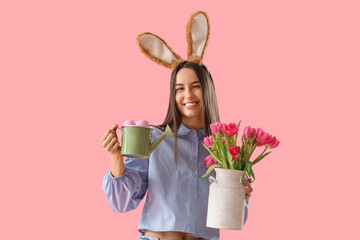 Young woman in bunny ears with tulips and Easter eggs on pink background