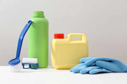 Concept of cleanliness, cleaning services. Green bottle and yellow canister decorated with blue brushes and blue rubber gloves on white background. Front view