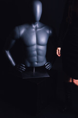 woman dressed in short black dress with black leather boots posing with male mannequin torso