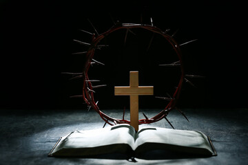 Crown of thorns with wooden cross, Bible and light on black grunge background