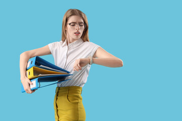 Stressed young businesswoman with folders looking at wristwatch on blue background. Time management...