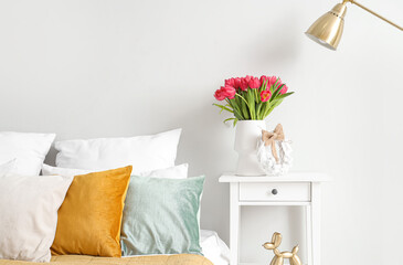 Vase with tulips and Easter wreath on table in light bedroom