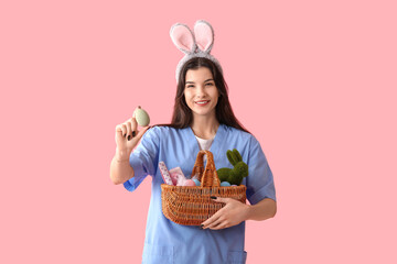 Female doctor in bunny ears with Easter eggs on pink background