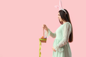 Young pregnant woman in bunny ears with Easter eggs on pink background