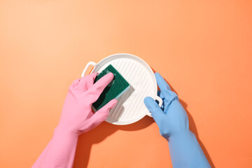Two hands wearing rubber gloves of two different colors are washing a ceramic plate with a sponge on a red background. Cleaning concept for ads.