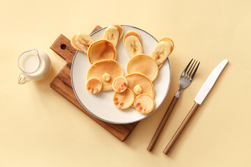 Funny Easter bunny pancakes and jug of milk on yellow background