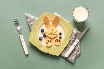 Funny Easter bunny pancakes with glass of milk on green background