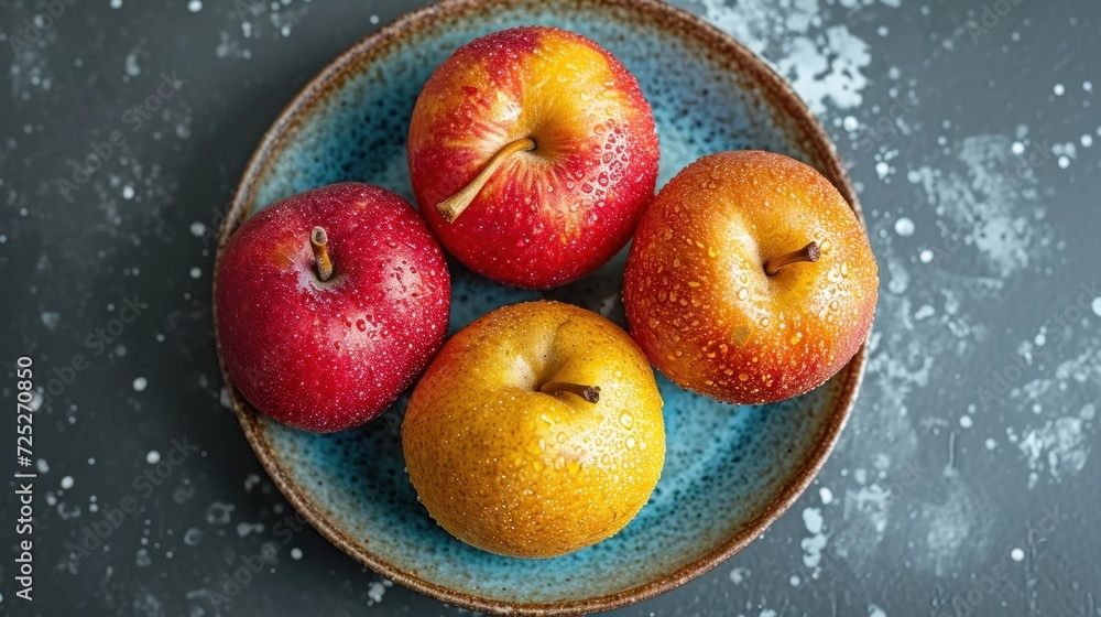 Poster three apples and two oranges on a blue plate on a gray surface with sprinkles on the surface.