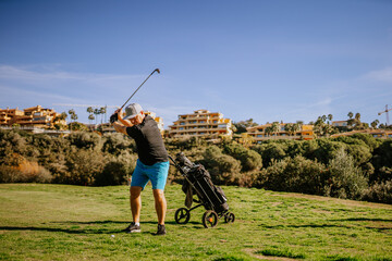Sotogrante, Spain - January 25, 2024 - Golfer in mid-swing with a golf cart on the grass and...