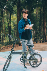 Young handsome bearded man taking a break while travelling the city with his bicycle using his digital tablet looking away thoughtfully