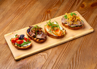 Bruschetta set with salmon, meat and vegetables on a wooden background