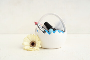Basket in shape of Easter egg with different lipsticks and flowers on white background