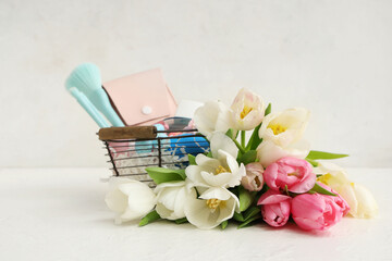 Basket with decorative cosmetics, Easter eggs and bouquet of tulips on white background