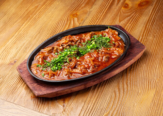 Beef in sauce in a frying pan on a wooden background