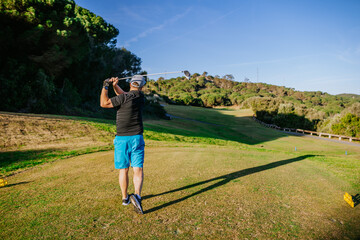 Sotogrante, Spain - January 25, 2024 - Man swinging a golf club on tee off area with grass and trees in background.