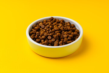 Bowl with dry pet food on yellow background studio shot