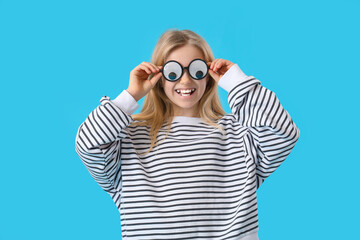 Little girl in funny eyeglasses on blue background. April Fools' Day celebration