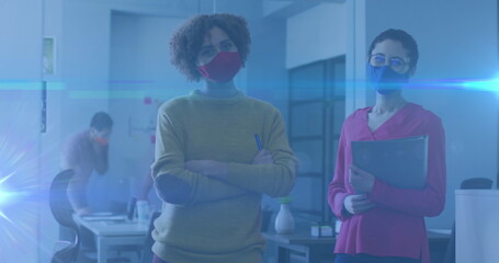 Image of glowing light trails over women in office talking and wearing face masks