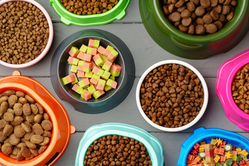 Various pet bowls with dry food on gray wooden background