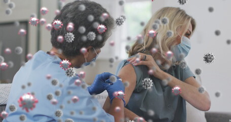 Image of covid 19 cells over woman receiving vaccination wearing face mask