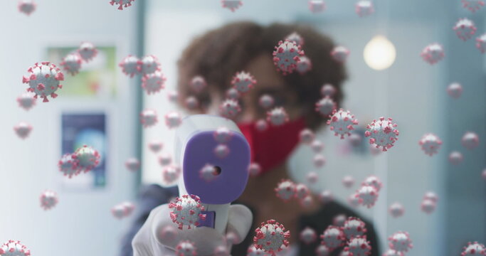 Image of covid 19 cells over woman using digital thermometer, wearing face mask