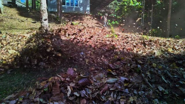Slow motion Gardeners simultaneously use a backpack blower. .Blow the leaves and grass clippings together into a large pile. .Keep your garden clean and prevent forest fires. clean park background.