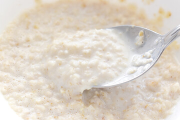 Oatmeal with milk on spoon in a bowl. Healthy and dietary breakfast. 