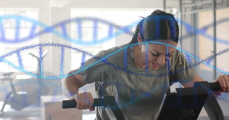 Image of dna strands over caucasian woman cross training on elliptical at gym