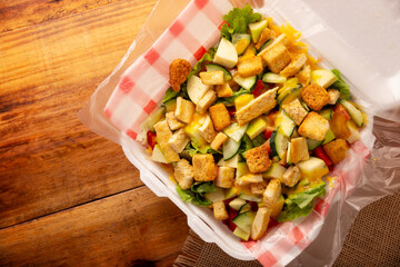 Healthy salad of lettuce, grilled chicken breast, cucumber, apple, croutons, honey mustard dressing and several other ingredients, served to go in a disposable Styrofoam container.