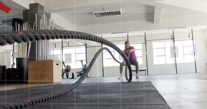 Image of graph processing data over caucasian woman cross training with battle ropes at gym