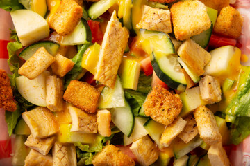 Healthy salad of lettuce, grilled chicken breast, cucumber, apple, croutons, honey mustard dressing and several other ingredients, Top view closeup, full screen.