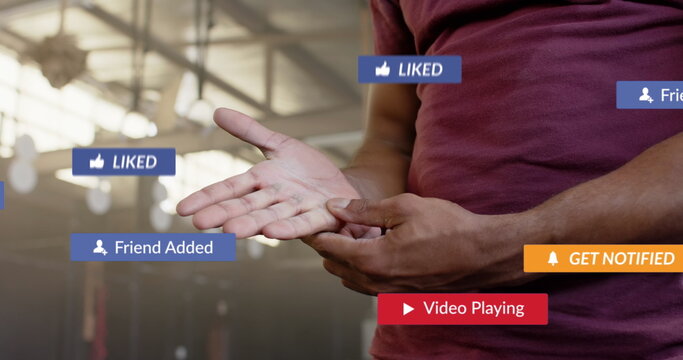 Image of social media notifications over african american man inspecting hand at gym