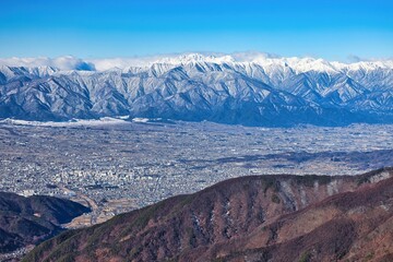 冠雪の北アルプスの穂高連峰と長野県松本市の街並み