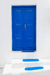 White facade of the house and blue door with stairs. Santorini island, Greece.