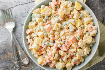 Delicious potato salad with green peas, carrots, corn and apple covered with mayonnaise close-up on...