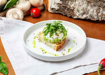 Toast with avocado, stracciatella and arugula on a plate on a wooden background