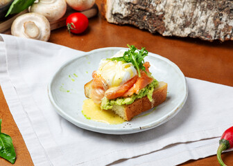 Toast with salmon, avocado and poached egg on a plate on a wooden background