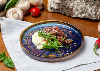 Beef tartare in a plate on a wooden background