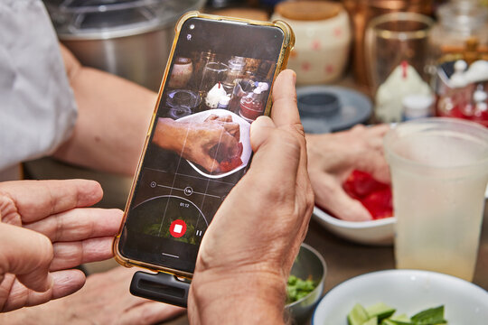 Woman using mobile phone to take pictures of dishes in kitchen for cooking recipe
