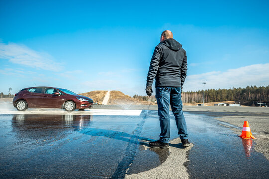 dynamic car braking test on wet road surface with water splashes and orange traffic cones, vehicle safety evaluation in controlled skidpan environment