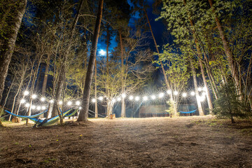 enchanted forest campground with hammocks under starburst lights, a tranquil outdoor retreat...